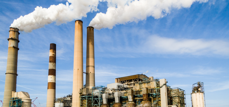 Industrial power plant with multiple smokestacks emitting white smoke against a blue sky.