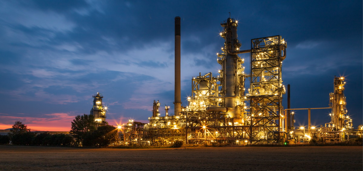 Oil refinery at night with illuminated structures against a dark blue sky.